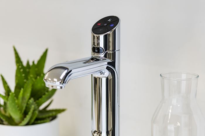 A silver HydroTap next to a jug and plant.