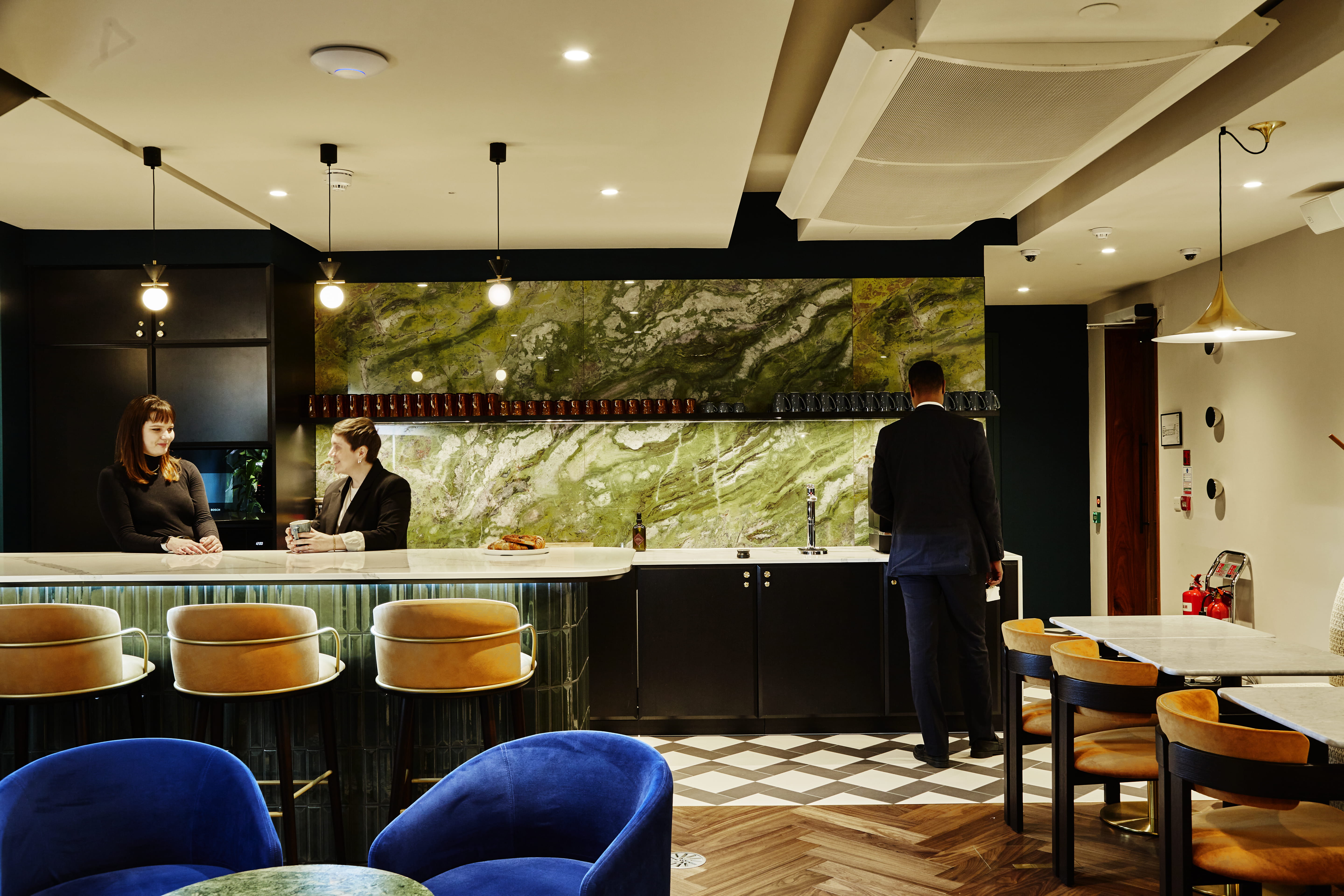 A black and green office kitchen with workers chatting over coffee.