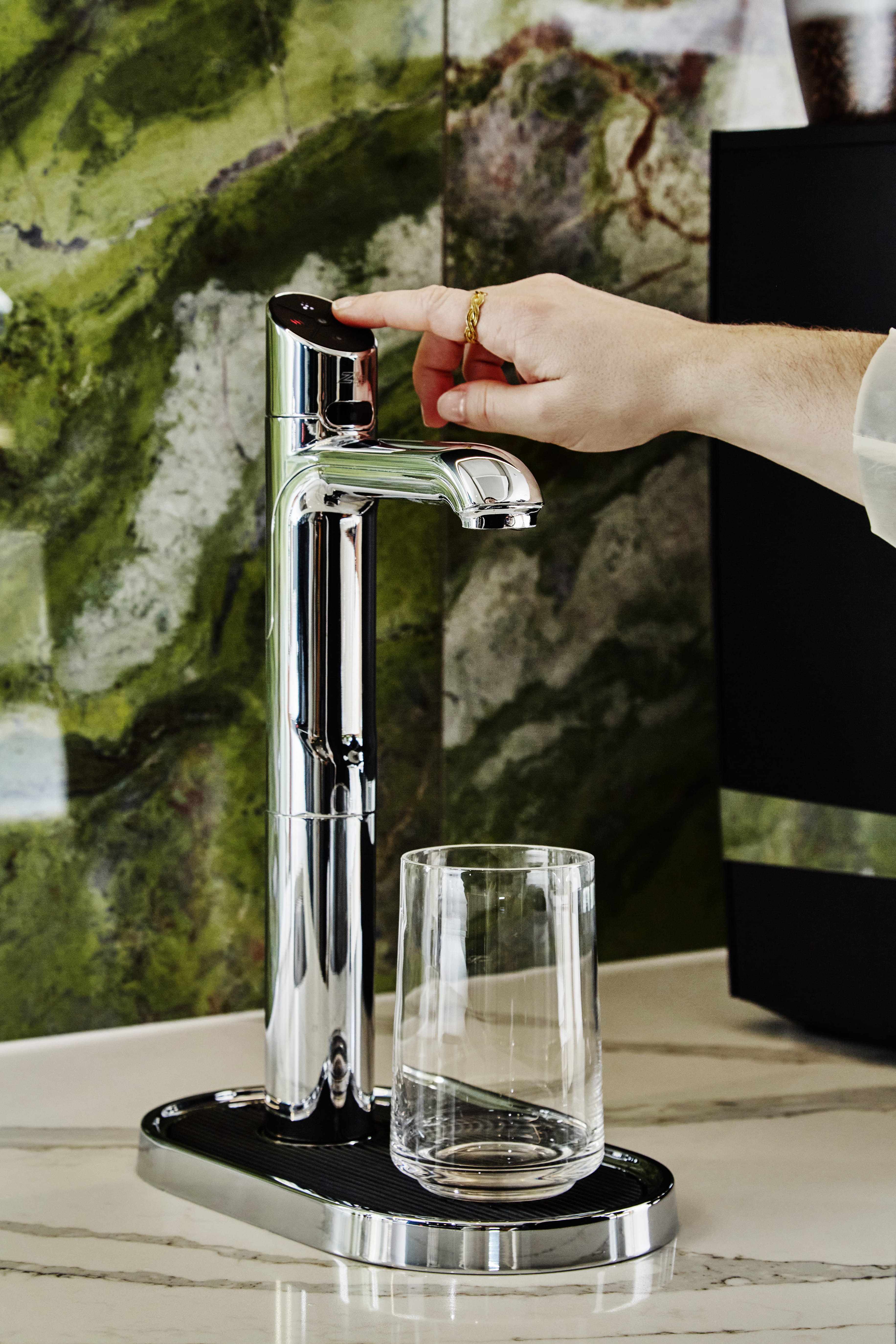 A silver HydroTap with a glass and a green background