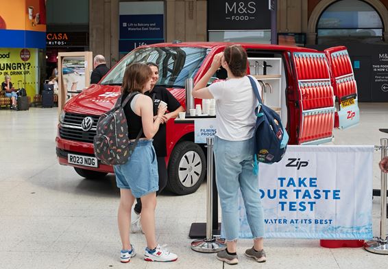two people tasting water in front of a Zip Water branded van