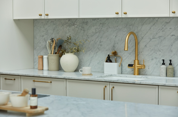 Minimalist kitchen with white marble walls, minimal decor, and a gold Zip HydroTap at the centre.